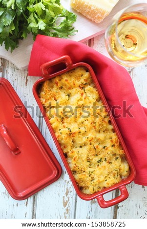 macaroni and cheese in red on a white table, a glass of wine