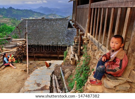 GUIZHOU PROVINCE; CHINA - APRIL 10: 7 years old boy near a wooden house in the village of ethnic minority Miao, April 10, 2010. Basha Miao Village, Congjiang County, Southeast Guizhou, Southwest China