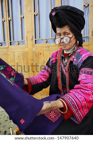 GUANGXI PROVINCE, CHINA - APRIL 4: Old woman in big glasses, red Yao nationality, ethnic minority groups in China,  holding a blue cloth with patterns embroidered by hand, April 4, 2010.