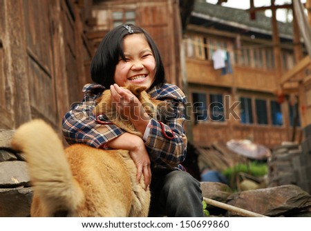 GUANGXI PROVINCE, CHINA - APRIL 3: Unidentified Chinese girl 8 years old, hugging red dog, village Dazhai, near Longsheng, April 3, 2010. Chinese teen girl plays with the ginger dog, near wooden farmhouse.