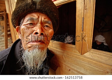 GUIZHOU PROVINCE, CHINA - APRIL 12: The elderly villager from the Chinese village of ethnic minorities, April 12, 2010. Asian old man in a fur hat, a blind right eye and with a gray goatee.