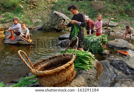 GUIZHOU PROVINCE, CHINA - APRIL 11: Asian family, two women and four children, are in middle of rural river, adult Chinese women wash green plants, Zengchong Dong ethnic Village, April 11, 2010.