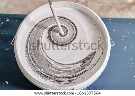Handyman is mixing black and white colors using painting mixer in the basket to get a gray color. Worker mixes paints with help of drill. Foto stock © 