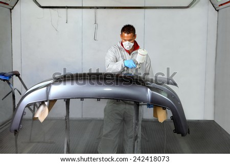 Saint Petersburg, Russia - June 26, 2014: Painting bumper car spray booth auto repair shop, working in a protective mask and clothing, operates a spray gun.