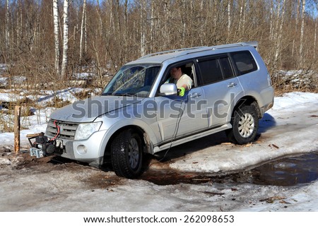 Nazia village, Leningrad Region, Russia - March 17, 2015: Vehicle is stuck in the forest creek in an ice wood road, the driver uses a winch with remote control to pull the car out of the pit.