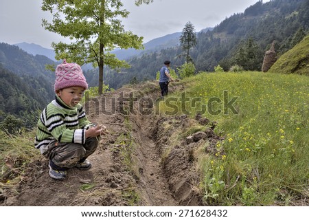 Langde Village, Guizhou, China - April 15, 2010: Rural China, mountainous terrain, unidentified boy about 4 years old is sitting near a farmer\'s field, his father works the soil.