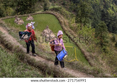 Langde Village, Guizhou, China - April 15, 2010: Two Asian women peasants, farmers go for agricultural work is carried on the shoulders of the yoke with the equipment for spraying plants.