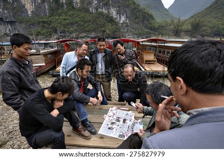 Yang Di village, Yangshuo, Guangxi, China - March 29, 2010: Chinese boatmen men playing cards near pier on background of karst hills,  Li River, Guangxi Zhuang autonomous region , southern China.