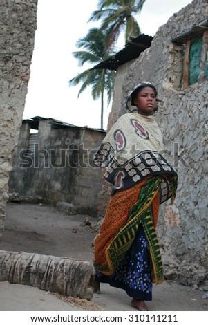 Zanzibar, Tanzania - February 20, 2008: Unknown barefoot dark-skinned African Muslim girl in head scarf, is on a narrow street fishing village.