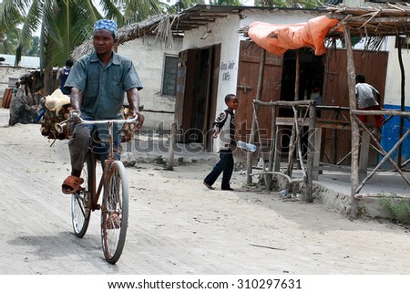 Zanzibar, Tanzania - February 16, 2008: Unknown black African men in the Arab skullcap, riding a bicycle on a dusty street in the fishing town.