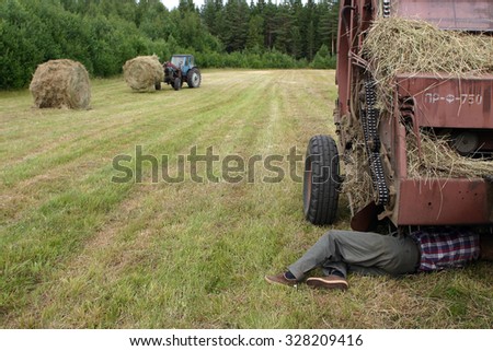 Lemozero, Olonets, Karelia, Russia - July 26, 2006: Farmer repairing tractor in field, during hay.