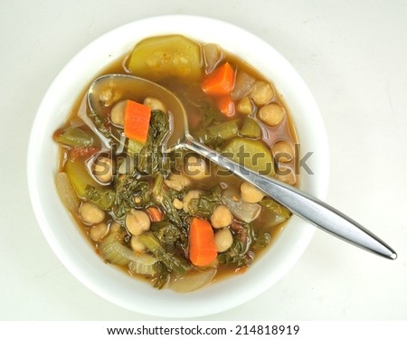 White bowl of minestrone soup with a spoon on a light background.