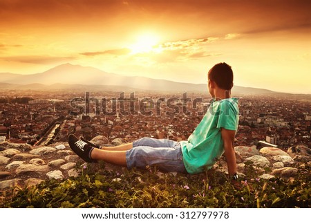 young relaxing boy looking to the city in the sunset atmosphere