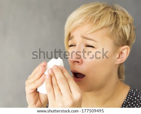 young woman sneezing into handkerchief