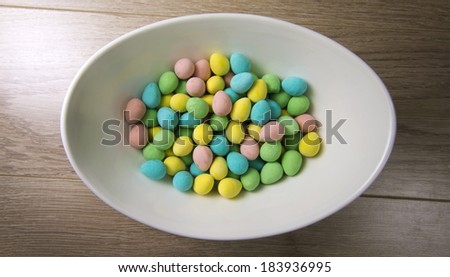 Colorful mini chocolate eggs in an egg shaped bowl sitting on a wood texture background