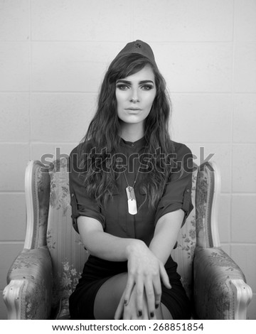 Portrait of a beautiful woman wearing a Soviet military hat and dog tags sitting on a chair in black and white