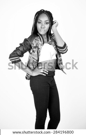 Beautiful black woman posing in a studio wearing a white tube top, camo jacket, heels and jeans in black and white.