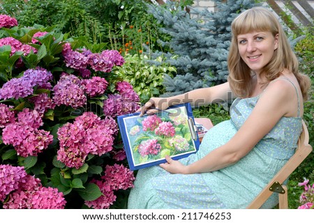 The young pregnant female artist shows drawing of a blossoming hydrangea in a garden