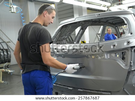 KALININGRAD, RUSSIA - SEPTEMBER 16, 2014: The young worker drills an opening in a car body a pneumodrill. Car assembly enterprise