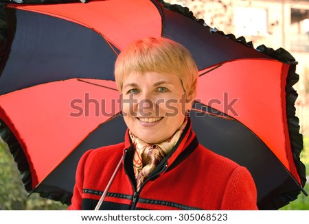 The woman of average years costs under a black-red umbrella