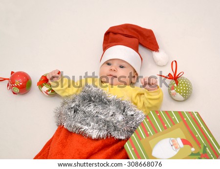 The baby in a New Year\'s suit of Santa Claus with Christmas tree decorations on a light background