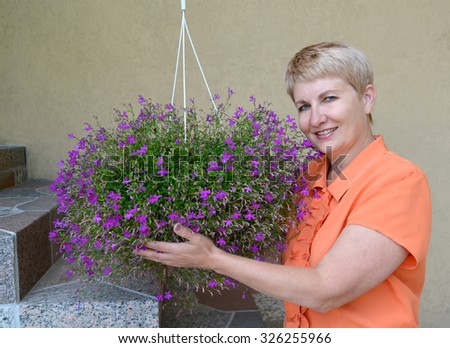 The joyful woman of average years supports a cache-pot with decorative flowers a lobelia
