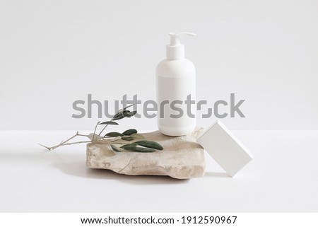 Set of cosmetic products on light background. White plastic pump bottle for shampoo, lotion mockup on stone podium. Blank soap box. Green olive tree branch. Healthy cosmetology, spa treatment concept.
