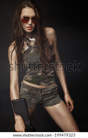 Beautiful brunette model with gun posing in full growth in studio