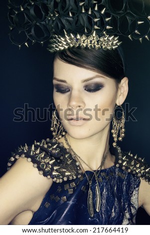 Portrait of gorgeous brunette woman in blue dress and headwear with spikes against dark background