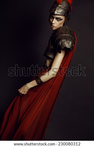 Fashion studio shot of beautiful woman in armor and in helmet with feathers on her head on black background