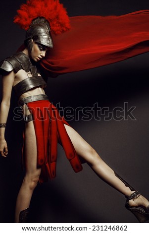 Fashion studio shot of beautiful woman in armor and in helmet with feathers on her head on black background