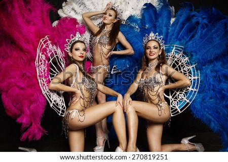Three beautiful women in crowns and carnival dresses with feathers on black background