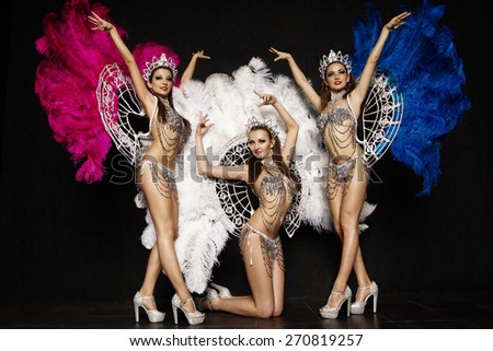 Three beautiful women in crowns and carnival dresses with feathers on black background