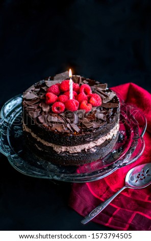A single lit candle glows atop a decedent chocolate layered cake with raspberries Imagine de stoc © 
