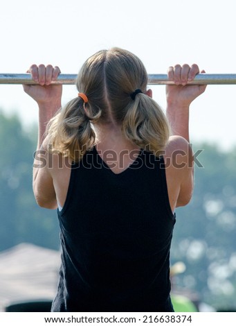 An active little girl works out doing pull ups on a metal bar exercise