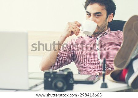 freelancer at work. happy man drinking coffee and looking at a computer. toned photo. morning designer