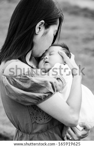 Black and White Asian mother kissing the cute baby in playground