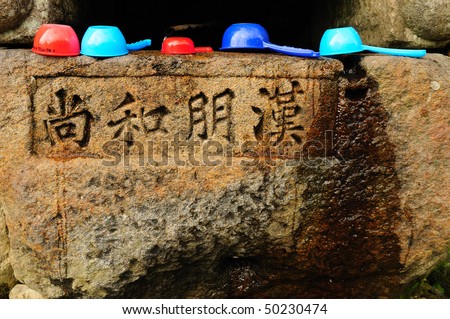 A drinking fountain with ancient text engraved on the rock and drinking cups on top. Taken at a South Korean temple.