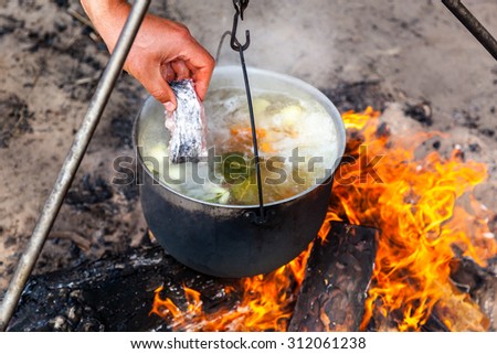 fish soup cooking in a pot on a fire in the forest by the sea