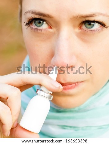Closeup of a blue eyed sick woman using nasal spray.