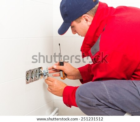 Electrician in protective workwear installing current outlet.