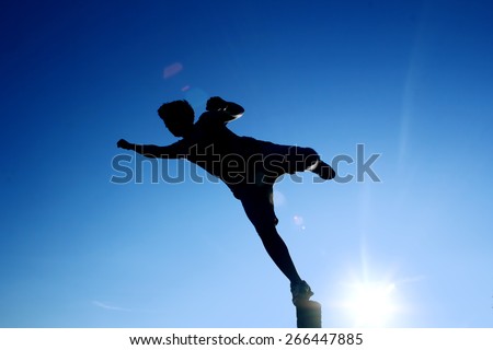 A one man silhouette jumping flying kicking playing, with blue sunny sky on background