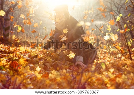 Portrait of a happy man playing with autumn leaves in forest. Retro style lens filter shot. Autumn background with sun flare light leak effect. Golden autumn