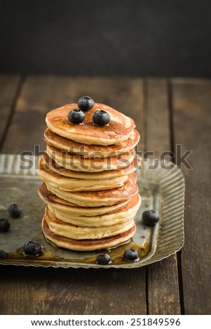 Pancakes with blueberries piled up on dark wooden background