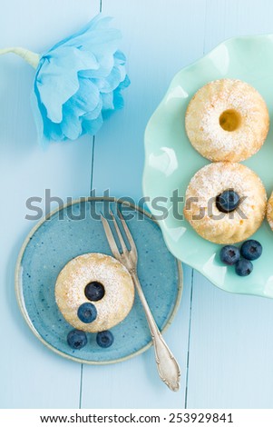 Mini bundt cakes with icing sugar on a cake stand with blueberries and a paper flower