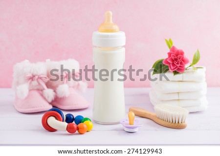 Baby bottle, pacifier, hairbrush, diapers, booties and rattle on pink table