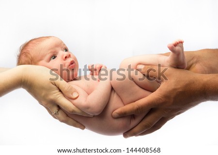 A newborn baby, held by the hands of both parents, lies alert and awake