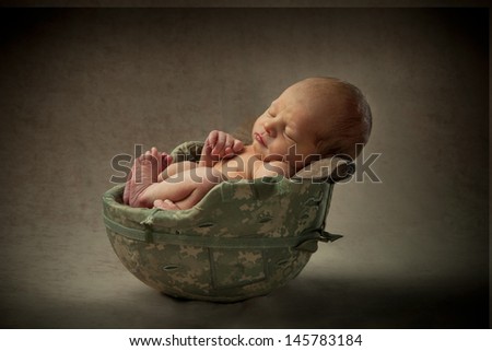 A newborn baby sleeps tucked inside his father\'s army helmet