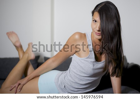 woman is tugging her shorts on grey lounge sofa and white wall
