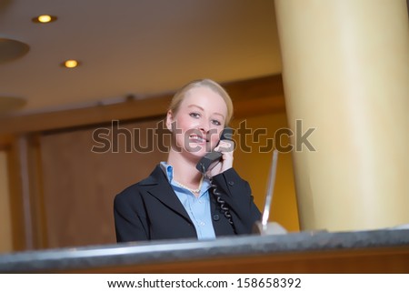 Beautiful blond woman wearing a suit answering an office telephone at work